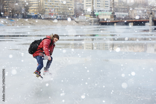 a young guy skating on a city ice rink on a frozen pond or river.