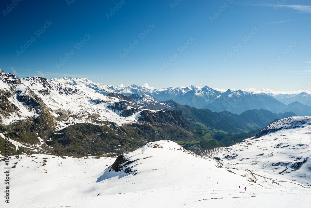 Wide angle view of a ski resort in the distance with elegant mountain peaks arising from the alpine arch in winter season.