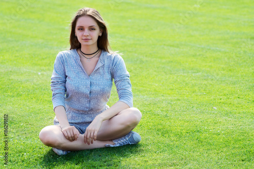 A beautiful young woman sits on a green lawn of a grass at a sports stadium. © Oleksandr Masnyi