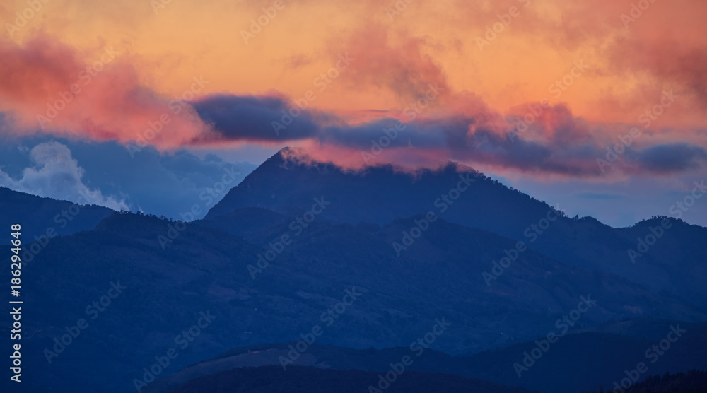 A view of the Costa Rican volcano in the clouds, lit by the setting sun. Quetzal forest after sunset. Los Quetzales National Park Nature Reserve. Costa rica.