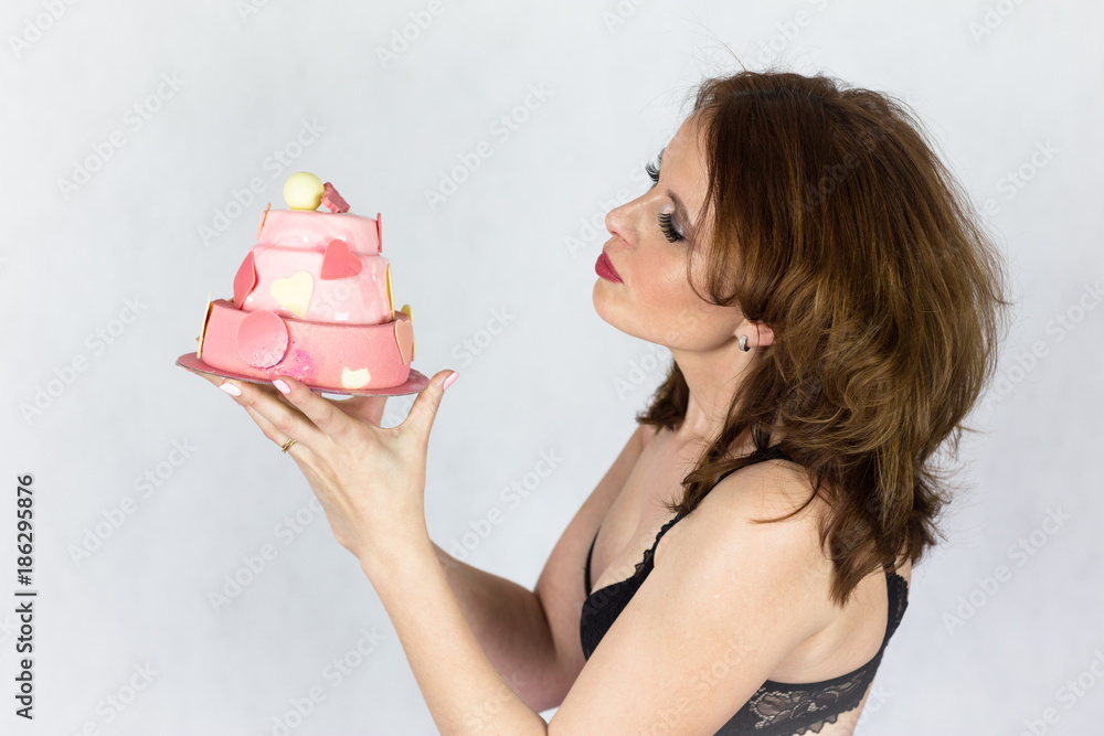 Slim, beautiful woman in black bra holding pink cake at her face