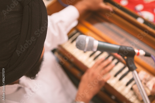 One Punjabi Singer with black turban is playing harmonium and singing at Gurudwara.