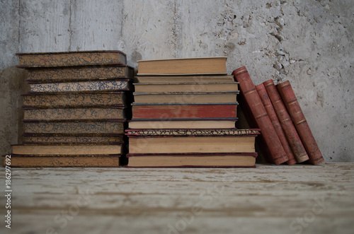 libri antichi appoggiati in verticale e orizzontali su tavolo legno e muro grezzo photo