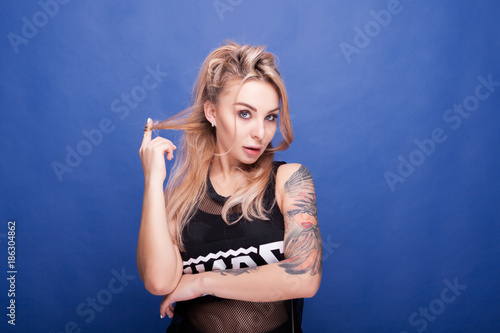 Kinky blonde tattooed woman looking straight to the camera on blue background © DC Studio