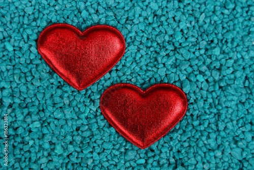 два красный атласных сердца лежат на синем песке