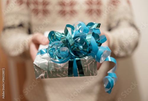 Man giving a Christmas present decorated with blue ribbon. Short depth of focus