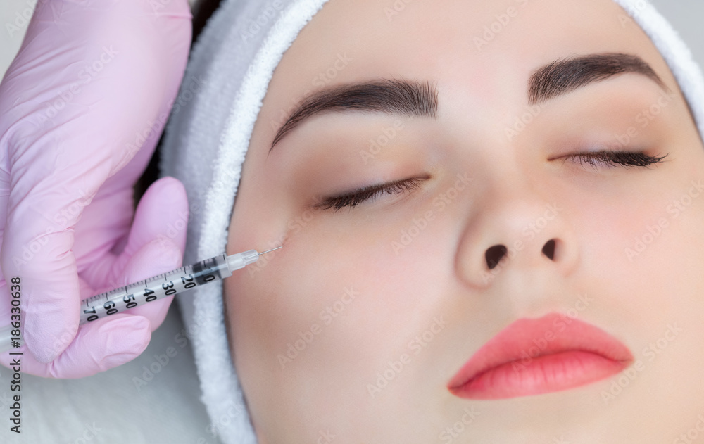 The doctor cosmetologist makes the Botulinum Toxin injection procedure for tightening and smoothing wrinkles on the face skin of a beautiful, young woman in a beauty salon.Cosmetology skin care.