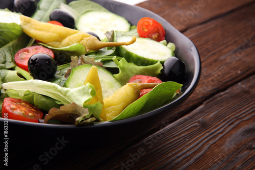 bowl of salad with vegetables and greens, with tomato, cucumber and onions.