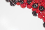 Blackberries and raspberries framed on white with copy space.  