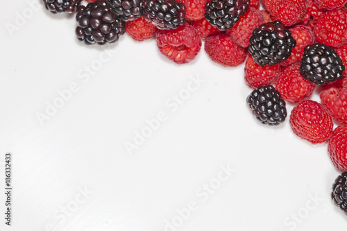 Blackberries and raspberries framed on white with copy space.  