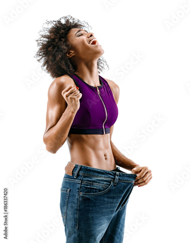 Sporty girl pulling her big jeans and showing weight loss. Photo of african girl on white background. Strength and motivation