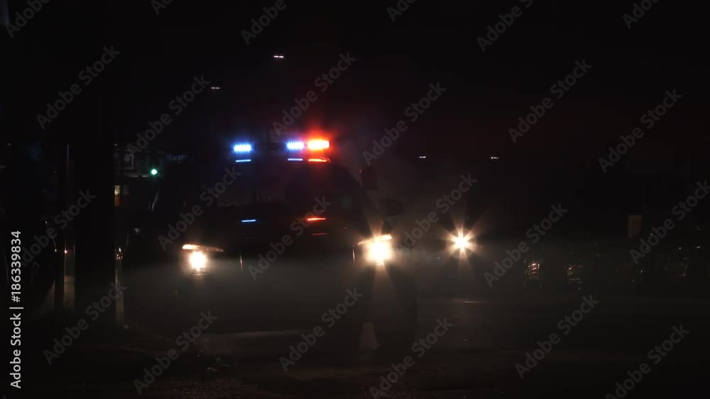 Dark city street traffic driving by parked police car at night have to stop for pedestrians crossing road. Dark city street traffic driving by parked police car at night have to stop for pedestrians crossing road.
