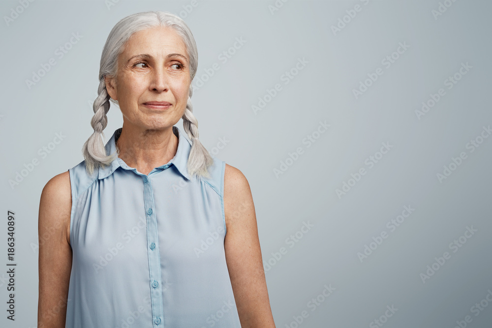 Positive happy smiling mature woman glad to recieve presents from children, looks aside, being thankful, isolated over light blue background with copy space for your advertising content. Emotions Positive happy smiling mature woman glad to recieve presents from children, looks aside, being thankful, isolated over light blue background with copy space for your advertising content. Emotions