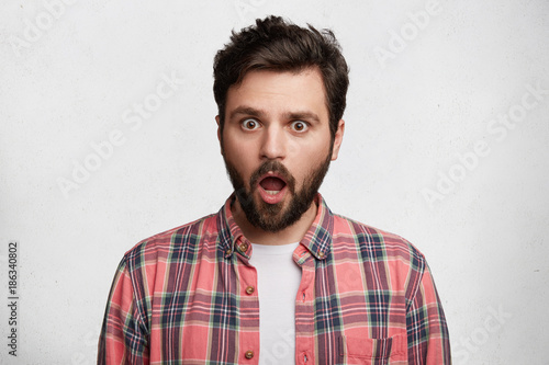 People, reaction and attitude concept. Emotional male with jaw dropped out, straes at camera, being stupefied to realize about his big failure or fault, isolated over white studio background