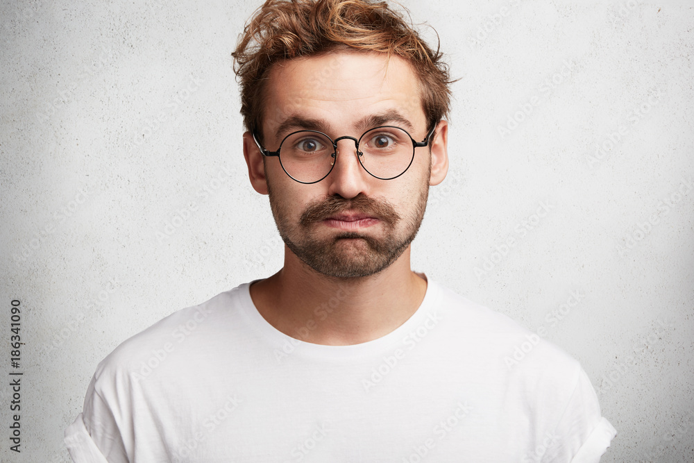 Portrait of tired stylish bearded intelligent male student gives deep sigh, presses lips, feels relief after passed exam, isolated over white background. Handsome young unshaven man poses indoor. Portrait of tired stylish bearded intelligent male student gives deep sigh, presses lips, feels relief after passed exam, isolated over white background. Handsome young unshaven man poses indoor.