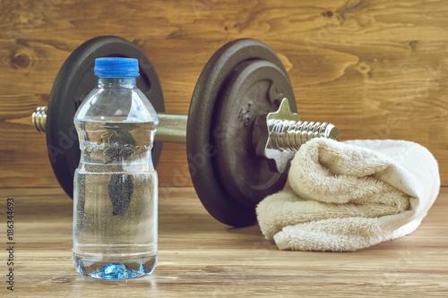 Fitness workout, slimming exercises, weight loss and diet healthy eating concept, dumbbells, bottle of mineral water and towel on wooden floor of training class