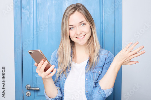 Excited female receives expected message or news on smart phone, looks happy at camera, has overjoyed expression. Positive young blond Caucasian woman glad to have a positive answer for her request.