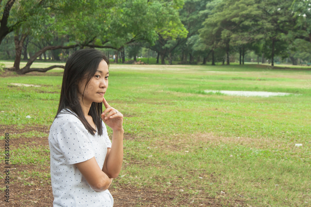 Woman wearing white t-shirt and standing on green grass in the park, she thinking something. Woman wearing white t-shirt and standing on green grass in the park, she thinking something.