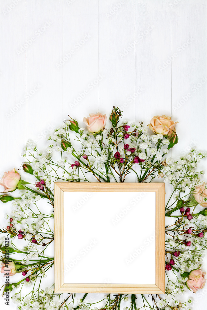 Beautiful flowers and wooden photo frame on white wooden table. Flat lay style