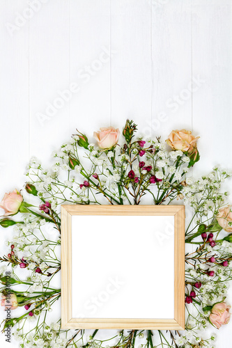 Beautiful flowers and wooden photo frame on white wooden table. Flat lay style