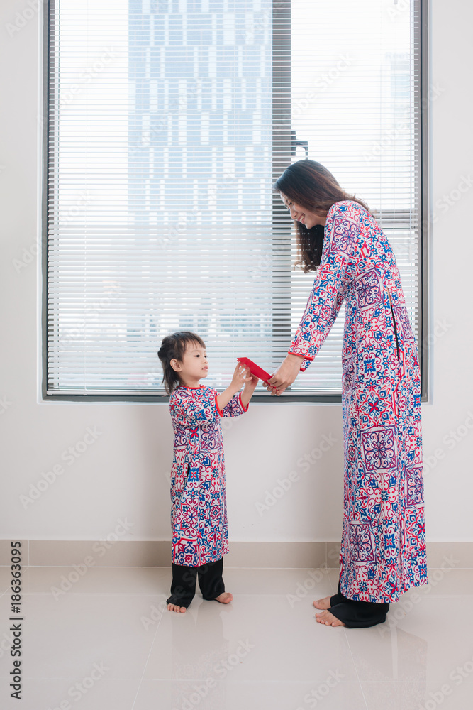 Vietnamese mother and daughter in Ao Dai Traditional dress, celebrate new year at home. Tet Holiday. Vietnamese mother and daughter in Ao Dai Traditional dress, celebrate new year at home. Tet Holiday.