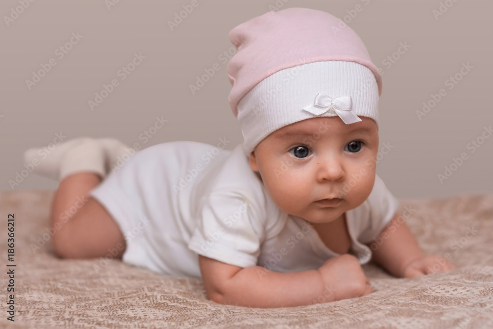 Charming beautiful lovely small female baby with plump cheeks creeps on bed, looks innocently on something, being naughty. Cute baby infant plays alone. Newborn kid crawls. Enthusiastic child Charming beautiful lovely small female baby with plump cheeks creeps on bed, looks innocently on something, being naughty. Cute baby infant plays alone. Newborn kid crawls. Enthusiastic child