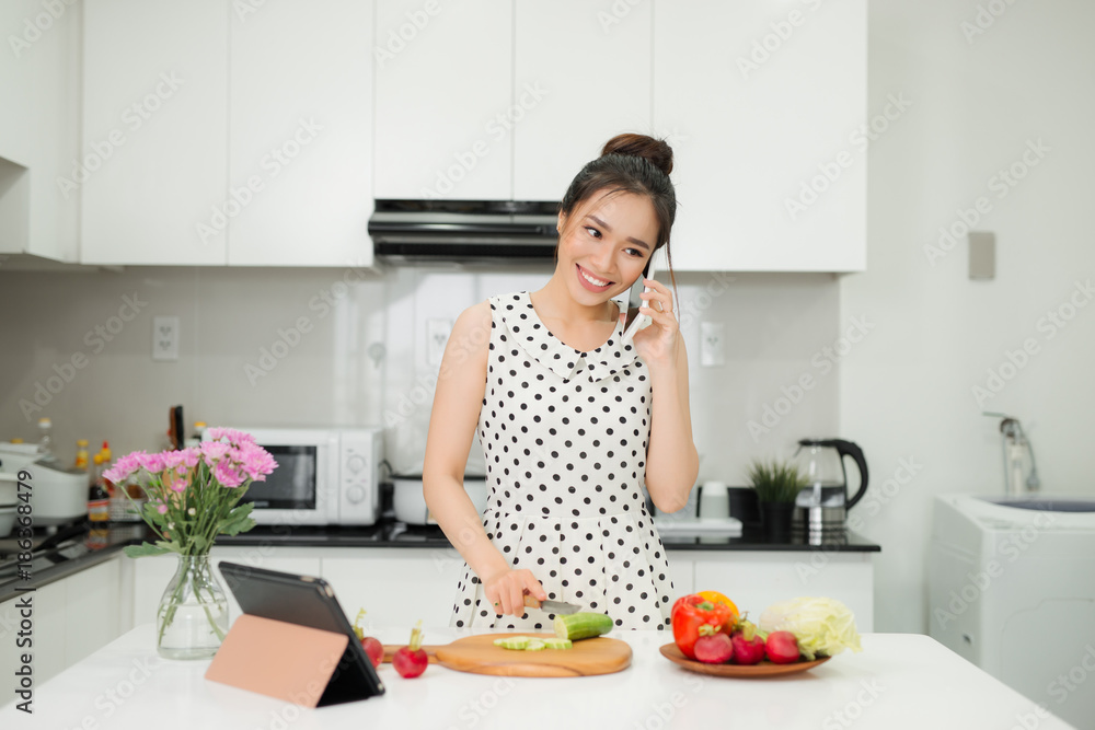 Young asian woman talking to phone and cooking for salad in the kitchen