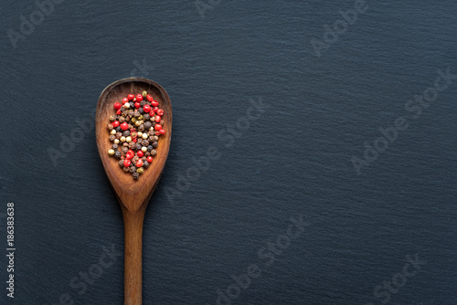 Wooden spoon filled with dried peppercorn on black background. Top view, copy space.