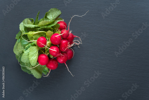 Bunch of radish with leaves on black background. Top view, copy space.