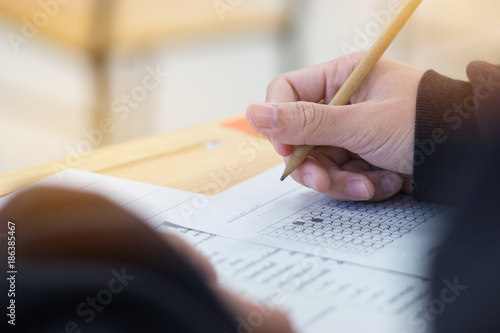 high school or university student hands taking exams, writing examination on paper answer sheet optical form of standardized test on desk doing final exam in classroom. Education literacy concept.