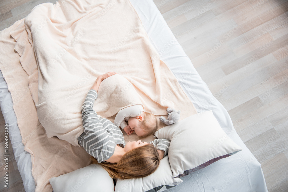 Top view of young female relaxing with child in an embrace. Baby is holding finger in mouth Top view of young female relaxing with child in an embrace. Baby is holding finger in mouth