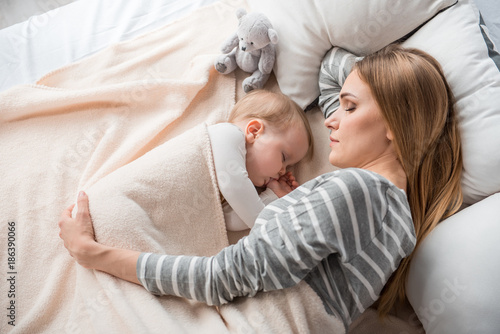 Top view of peaceful mother and cute child lying on double bed. They are sleeping together with tranquility
