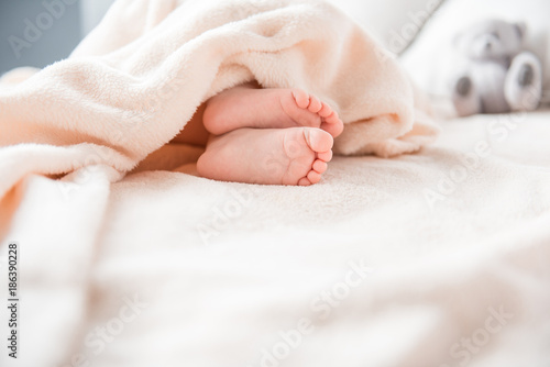 Close up of tender little feet resting on bed. Pink soft blanket is covering them. Focus on legs. Copy space