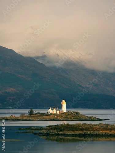 Isle Ornsay with white tower of Lighthouse; Isle of Skye; Scotland. Sunny winter day with snowy mountains photo