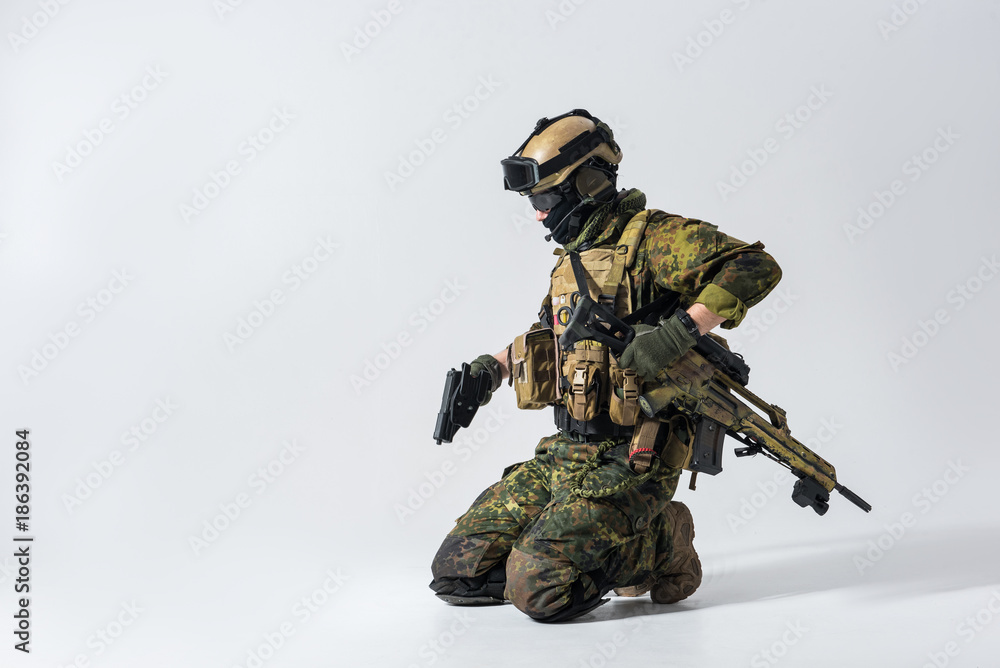 Side view serious defender holding pistol in arms while locating on knee. Protection concept. Copy space Side view serious defender holding pistol in arms while locating on knee. Protection concept. Copy space