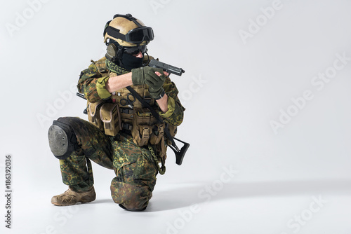 Portrait of serious defender kneeling while shooting with gun. Protection and attack concept. Copy space