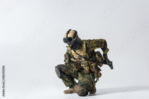 Full length portrait of serious soldier shooting with gun while taking assault rifle. War concept. Copy space