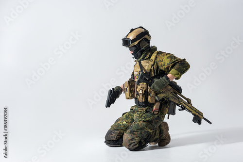 Side view serious defender holding pistol in arms while locating on knee. Protection concept. Copy space
