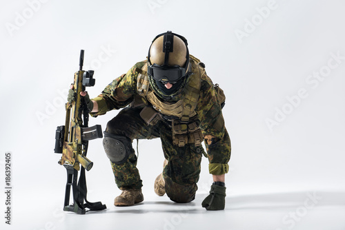 Portrait of stern defender rising from knees while leaning on weapon. Profession concept