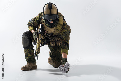 Portrait of serious defender taking toy from ground while looking at it. He holding assault rifle in hands. War and peace concept. Copy space