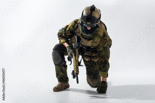 Portrait of tired soldier kneeling and leaning on arm while keeping modern weapon in hand. Military concept