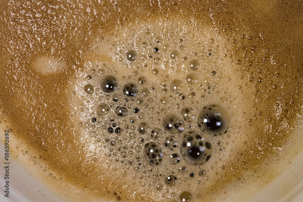 Obraz premium Fresh cup of Americano coffee seen close-up, showing the myriad of bubbles and thick froth. Part if the plan ceramic mug may be seen in this close-up image, taken in a well-known coffee franchise.