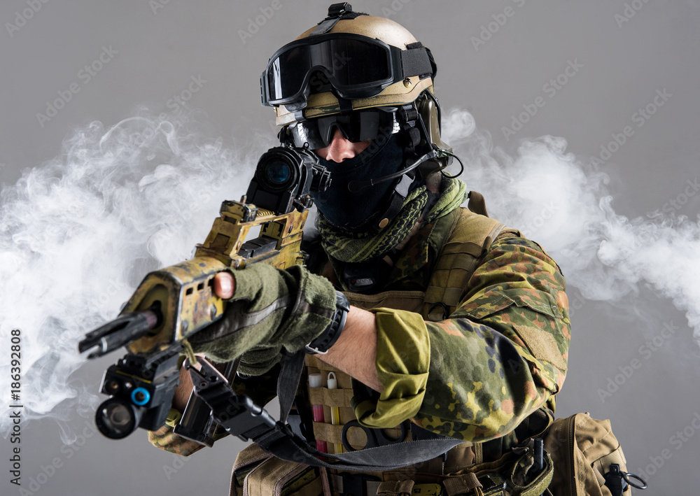 Fototapeta premium Portrait of serious soldier keeping assault rifle while standing in smoke. War concept