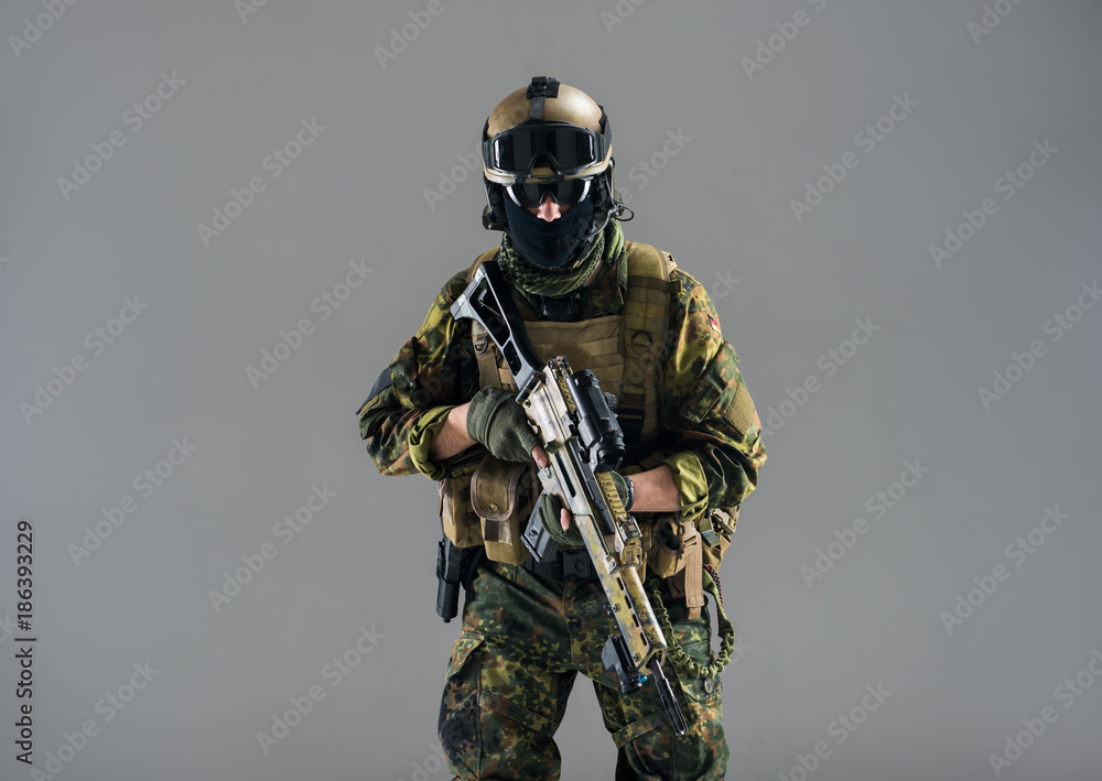 Portrait of stern male wearing military apparel while holding weapon in hands. Technology and war concept. Isolated Portrait of stern male wearing military apparel while holding weapon in hands. Technology and war concept. Isolated