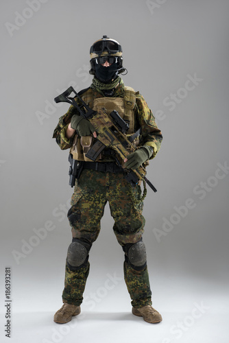 Full length portrait of stern soldier keeping assault rifle in hand. Army concept