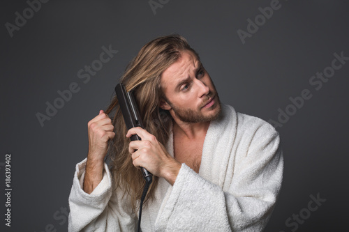 Waist up portrait of mature male in white robe taking care about his long hair. Isolated on grey background