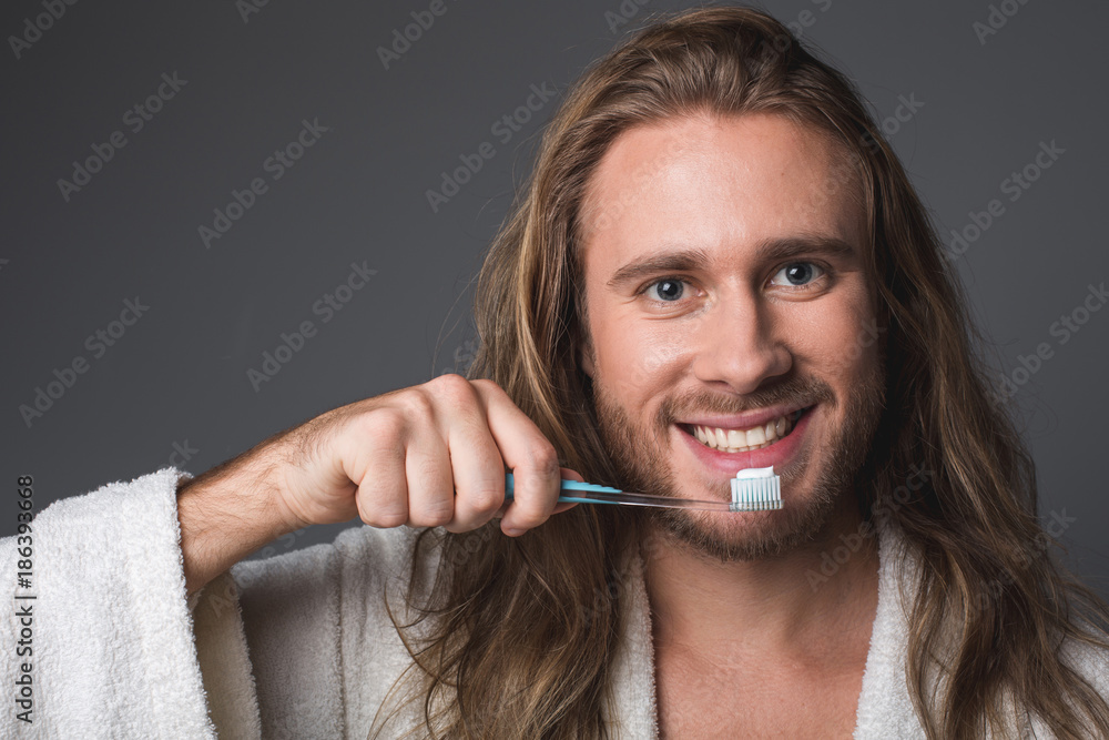 Healthy teeth. Portrait of smiling guy holding toothbrush in his hand. Isolated on grey background Healthy teeth. Portrait of smiling guy holding toothbrush in his hand. Isolated on grey background