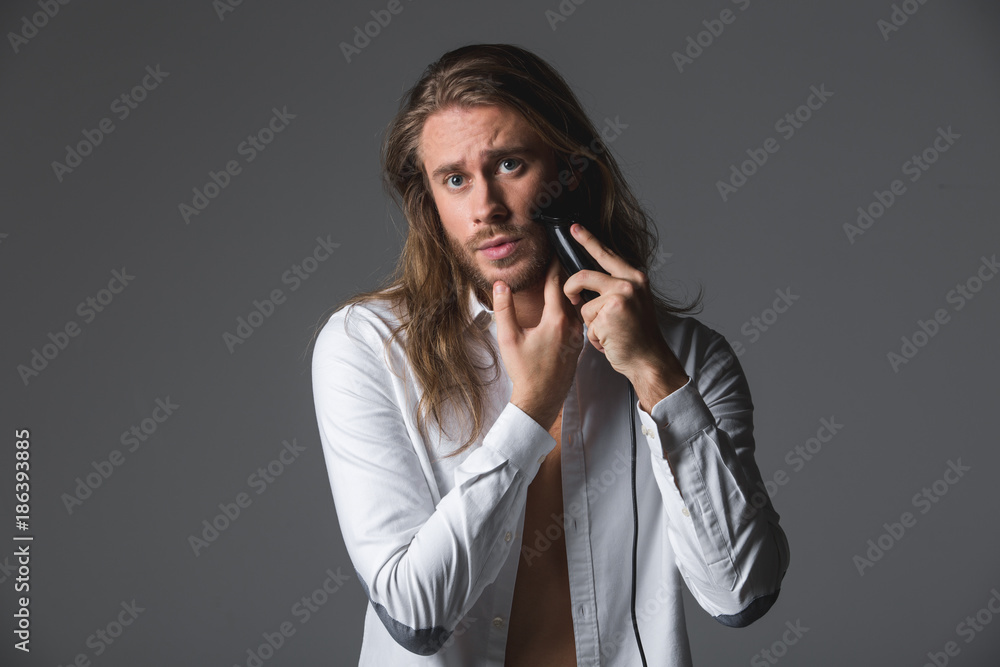 Waist up portrait of good looking man running razor along cheek. Isolated on grey background Waist up portrait of good looking man running razor along cheek. Isolated on grey background