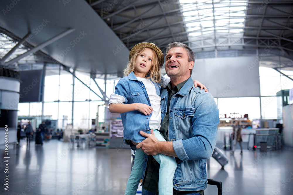 Pleasant mature father and his daughter are expressing astonishment while looking at something at international airport. Man is holding little girl on his hands. People in background Pleasant mature father and his daughter are expressing astonishment while looking at something at international airport. Man is holding little girl on his hands. People in background