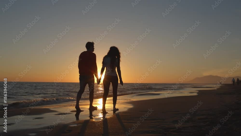 Young couple walking along beach in sunset holding hands Young couple walking along beach in sunset holding hands